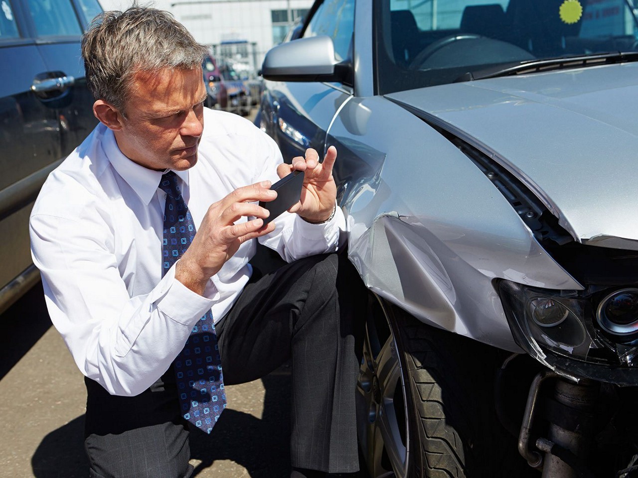 An insurance estimator taking pictures of a car's damaged front after an accident.
