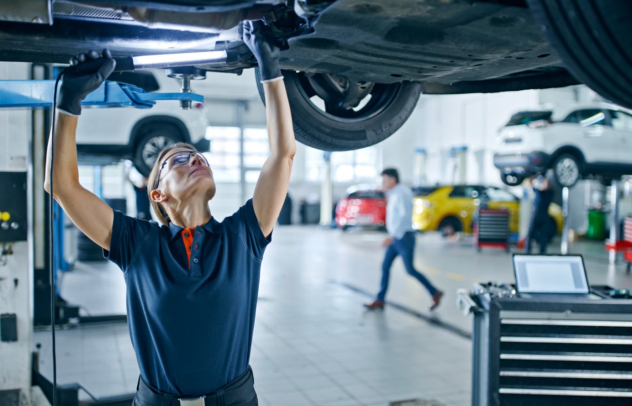 A female auto technician working under a car in an auto mechanic shop
