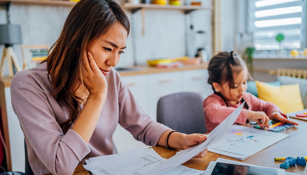Young stressed mother checking her finances while her daughter is playing next to her