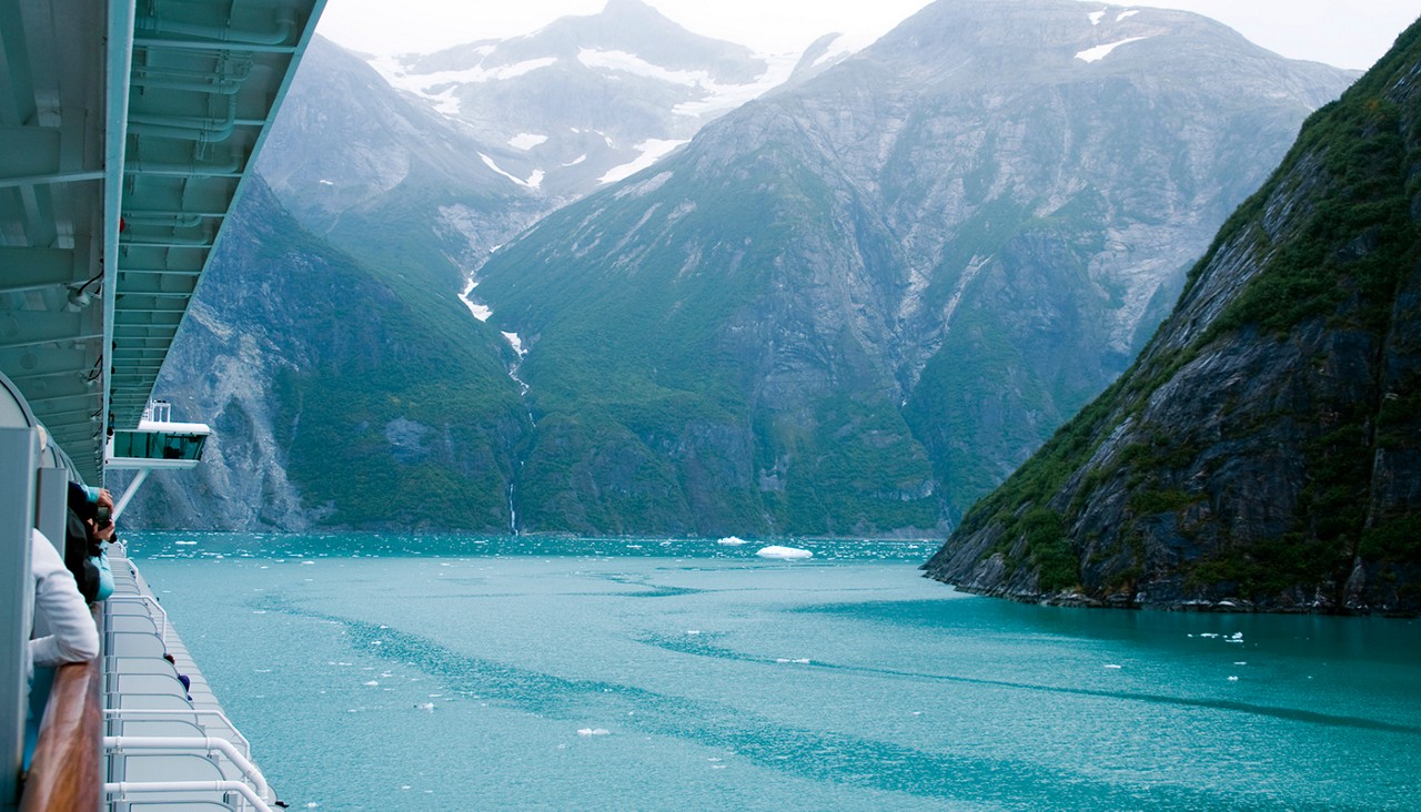 Near vertical mountain slopes carved by glaciers. The cold blue green waters of Tracy Arm Fjord in Alaska as viewed from a cruise ship.